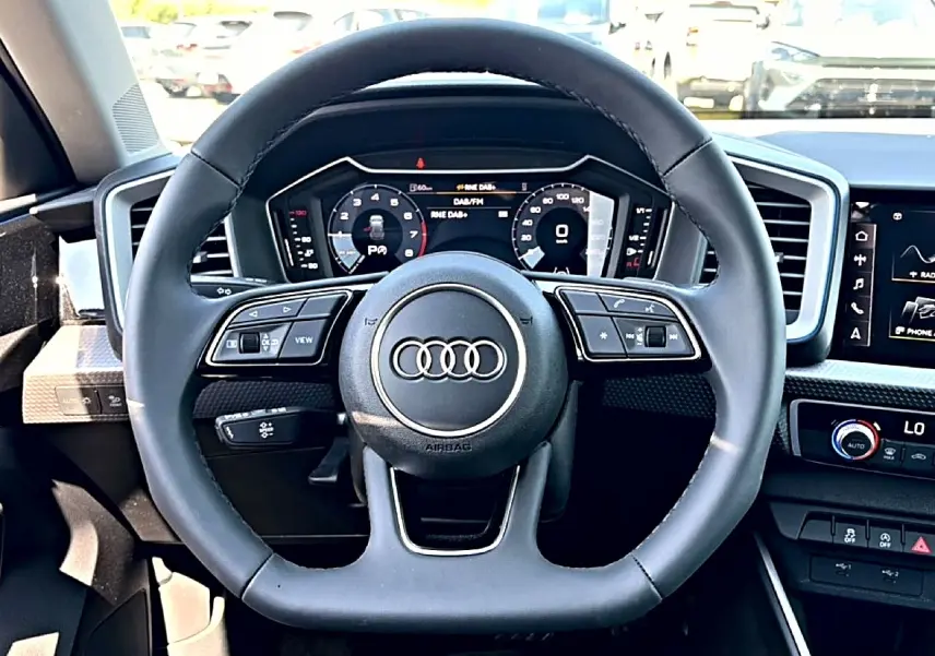 Vue frontale du volant cuir noir multifonction de l'Audi A1 Sportback avec tableau de bord digital et écran tactile.