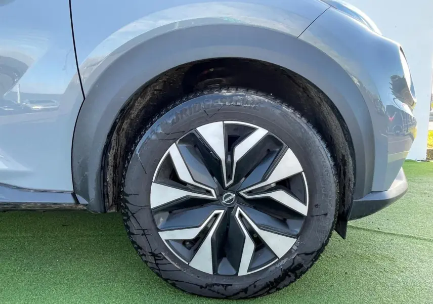 Gros plan sur la roue avant gauche du Nissan Juke 2024 gris ceramic avec jante alliage noire et argentée.