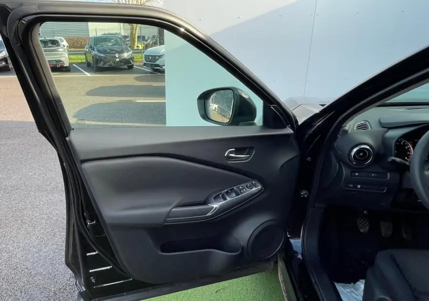 Intérieur côté conducteur du Nissan Juke II gris ceramic 2024, avec porte ouverte et commandes électriques visibles.