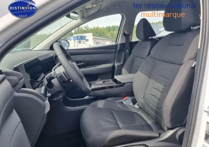 Vue intérieure côté conducteur du Hyundai Tucson blanc atlas 2025 avec sièges tissu noirs et tableau de bord moderne.