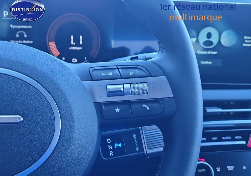 Gros plan sur le volant cuir noir du Hyundai Tucson blanc atlas 2025, avec commandes multifonctions et écran tactile en arrière-plan.