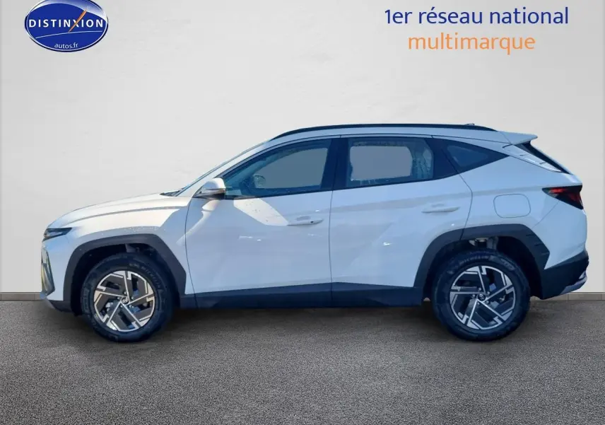 Profil côté gauche du Hyundai Tucson blanc atlas 2025 avec jantes alliage et barres de toit noires.