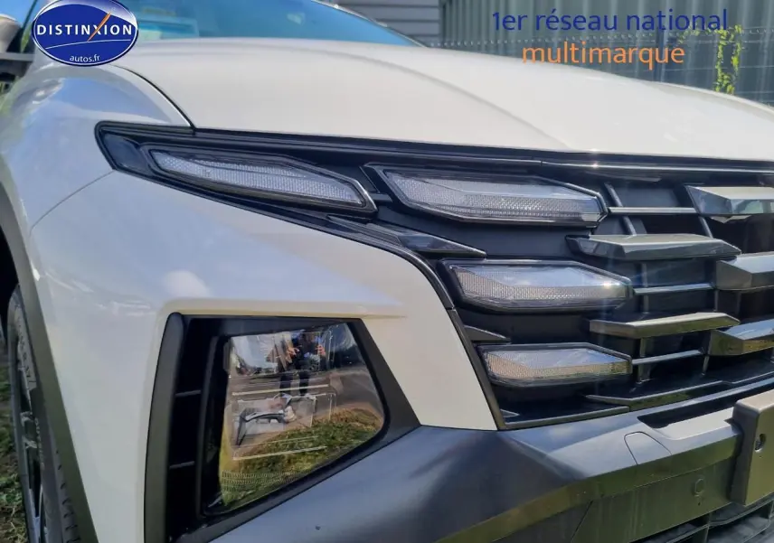 Gros plan sur l'avant droit du Hyundai Tucson blanc atlas 2025 avec calandre grise et feux LED distinctifs.