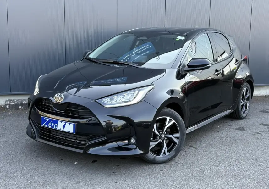 Toyota Yaris Hybride 2025 noir intense vue 3/4 avant avec jantes alliage et phares LED allumés.