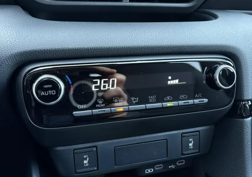 Gros plan sur la console centrale noire de la Toyota Yaris hybride 2025, affichant la climatisation à 26°C et les sièges chauffants activés.