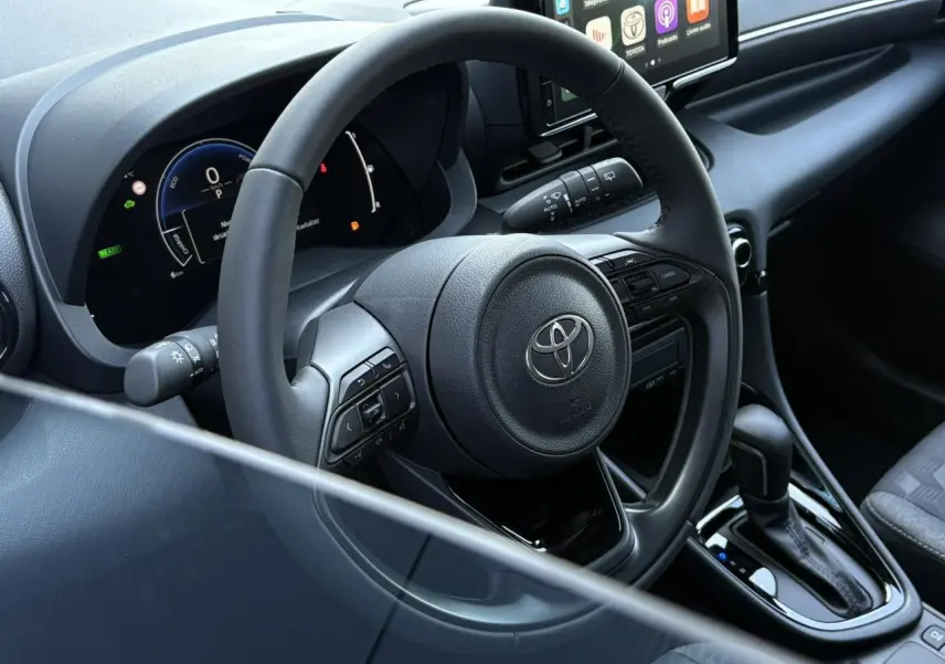 Vue intérieure centrée sur le volant cuir et tableau de bord numérique de la Toyota Yaris Hybride 2025.