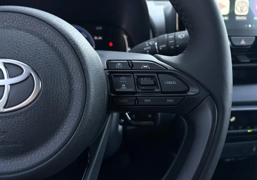 Gros plan sur le volant cuir noir de la Toyota Yaris 2025 hybride, montrant les commandes de régulateur adaptatif côté droit.