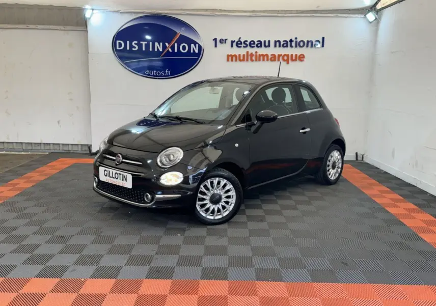 Fiat 500 noire vue en 3/4 avant droit dans un showroom avec jantes alliage et phares ronds allumés.