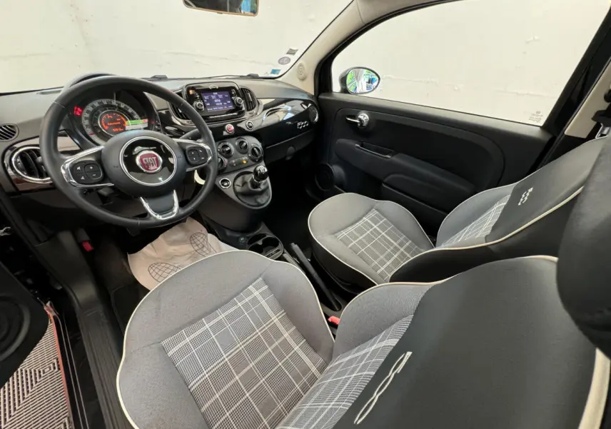 Vue intérieure avant droite de la FIAT 500 noire 2019, montrant le volant cuir, tableau de bord et sièges gris à motifs.
