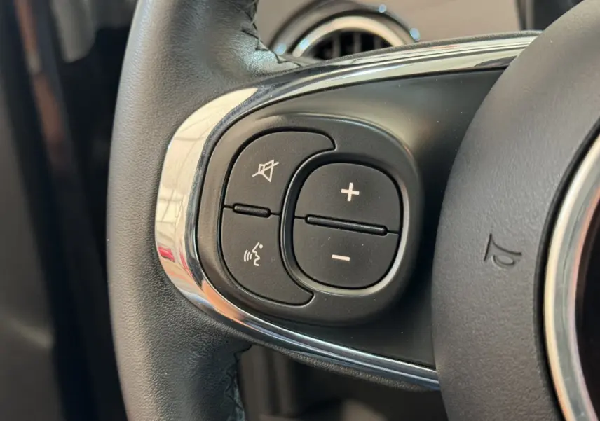 Gros plan sur les commandes audio au volant cuir d'une Fiat 500 noire, mettant en valeur les boutons de volume et de coupure du son.
