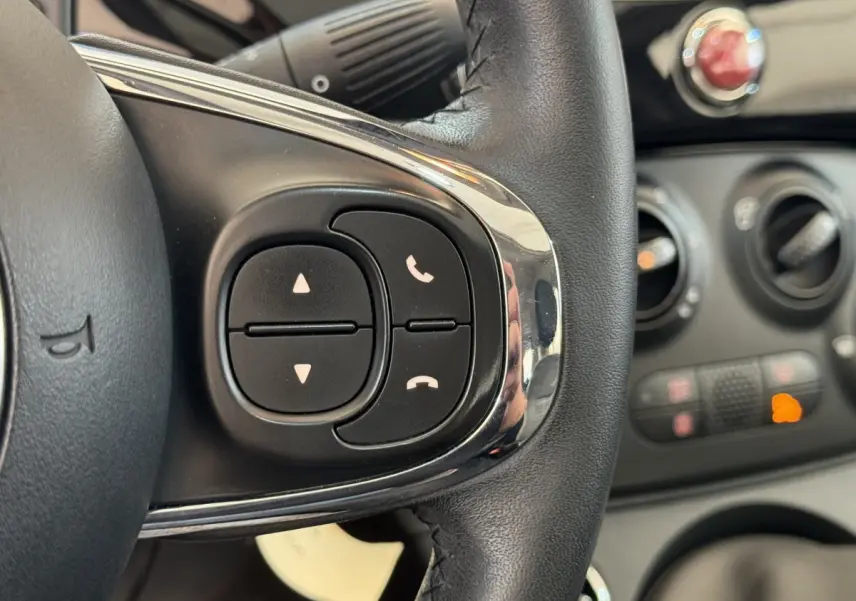 Gros plan sur les commandes du volant cuir noir de la Fiat 500 Lounge 2019 avec tableau de bord en arrière-plan.