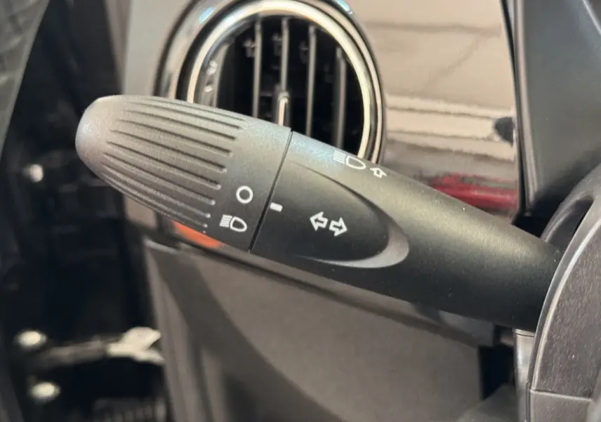 Gros plan sur la commande des clignotants et phares dans l'habitacle noir du Fiat 500 Lounge 2019.