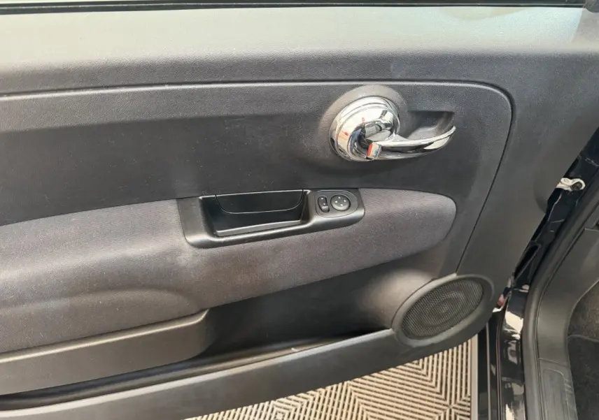 Gros plan sur la porte intérieure côté conducteur noire d'une FIAT 500 Lounge 2019 avec poignée chromée et commandes électriques.