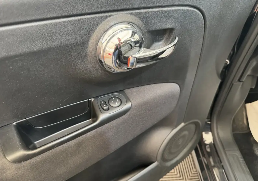 Gros plan sur la poignée intérieure chromée et les commandes de rétroviseurs du côté gauche d'une FIAT 500 noire de 2019.