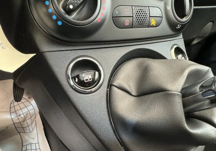 Gros plan sur la console centrale noire de la Fiat 500 Lounge 2019, montrant la commande de lève-vitre et le soufflet de levier de vitesses.
