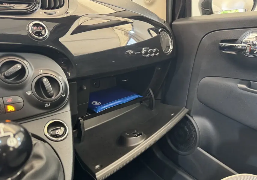 Intérieur de la FIAT 500 noire, vue côté passager sur la boîte à gants ouverte avec manuel bleu visible.