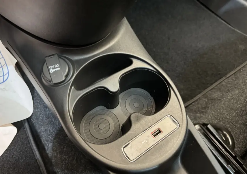 Gros plan sur la console centrale noire de la Fiat 500 Lounge 2019 avec prises USB et 12V et porte-gobelets.