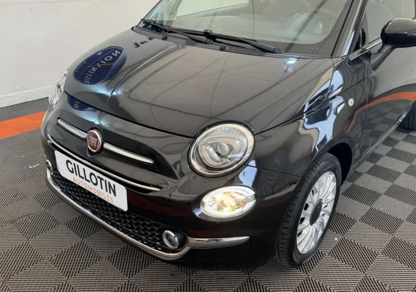 Vue 3/4 avant droite d'une FIAT 500 noire avec phares allumés et jantes argentées sur sol damier.