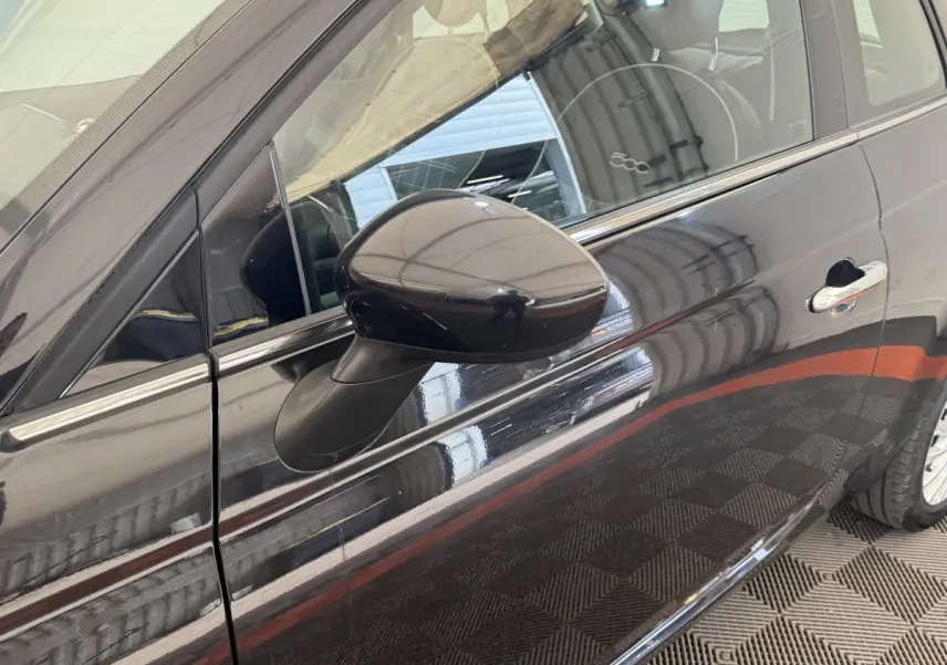 Gros plan sur le rétroviseur côté gauche d'une Fiat 500 noire 2019, avec reflet de l'intérieur et poignée chromée visible.