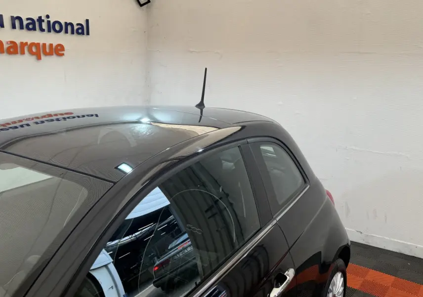 Vue 3/4 arrière droite d'une Fiat 500 noire brillante avec antenne de toit et poignées chromées visibles.