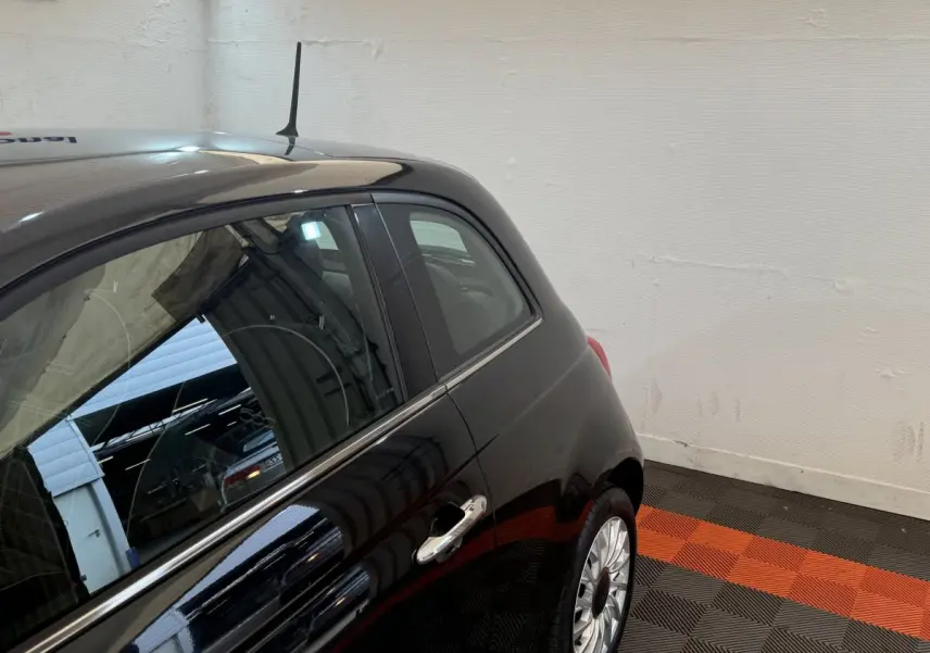Vue côté droit arrière d'une FIAT 500 noire brillante avec jante argentée dans un garage intérieur.