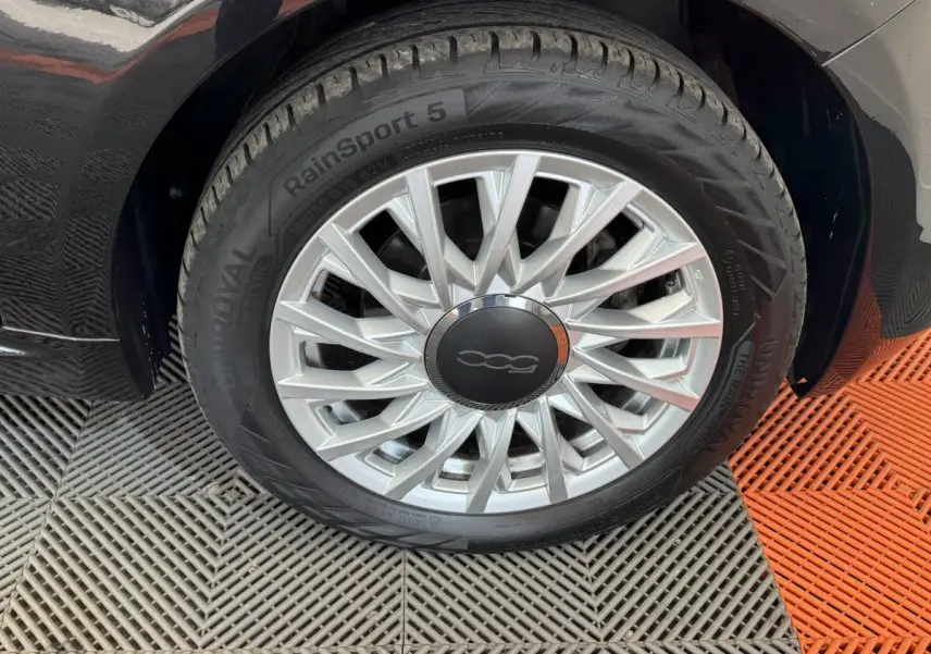 Gros plan sur la roue avant droite noire d'une FIAT 500 1.2 8V 69ch Lounge avec jante argentée à rayons fins
