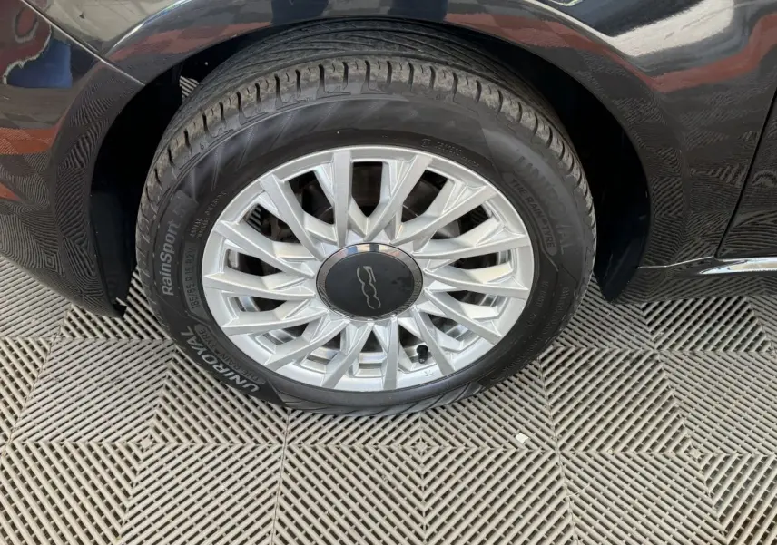 Gros plan sur la roue avant droite noire d'une FIAT 500 Lounge 2019 avec jante argentée au design étoilé.