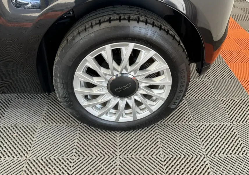 Gros plan sur la roue avant droite noire d'une FIAT 500 1.2 8V 69ch Lounge avec jante argentée à rayons fins.