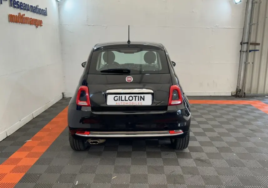 Vue arrière d'une FIAT 500 noire stationnée en intérieur sur un sol à damiers gris et orange.