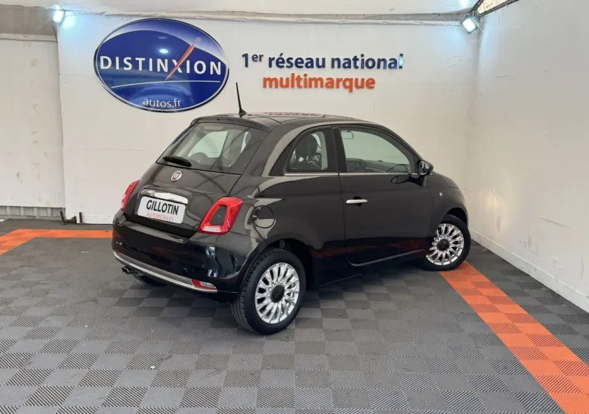 Vue 3/4 arrière droite d'une Fiat 500 noire 2019 dans un showroom avec jantes argentées et feux arrière LED.