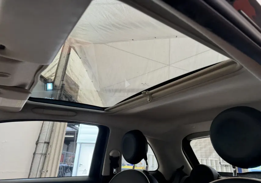 Toit panoramique ouvert vu de l'intérieur arrière droit de la Fiat 500 noire avec sièges avant ronds.