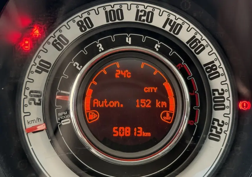 Gros plan sur le tableau de bord numérique orange d'une Fiat 500 noire, affichant la vitesse et l'autonomie.
