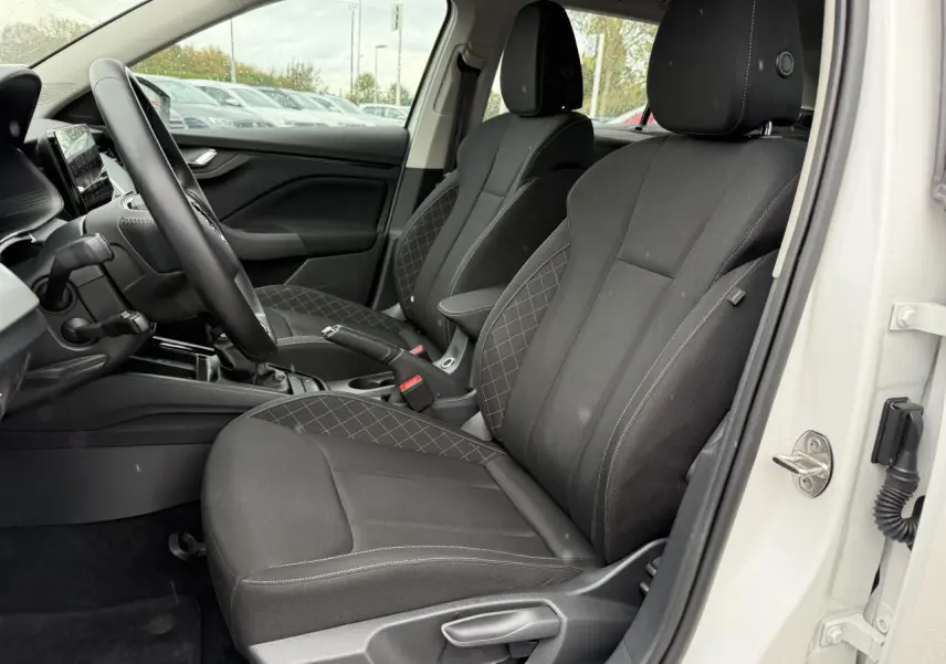 Vue intérieure côté conducteur d'une Skoda Scala blanche 2023, sièges noirs avec surpiqûres et console centrale visible.
