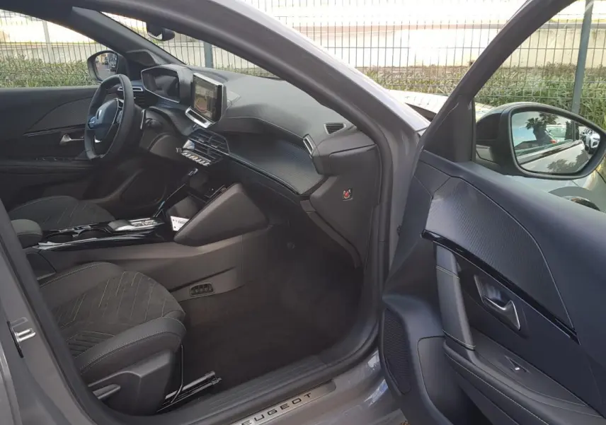 Vue intérieure côté conducteur de la Peugeot 208 Hybrid 110 e-DCS6 GT gris, avec tableau de bord et écran tactile visibles.