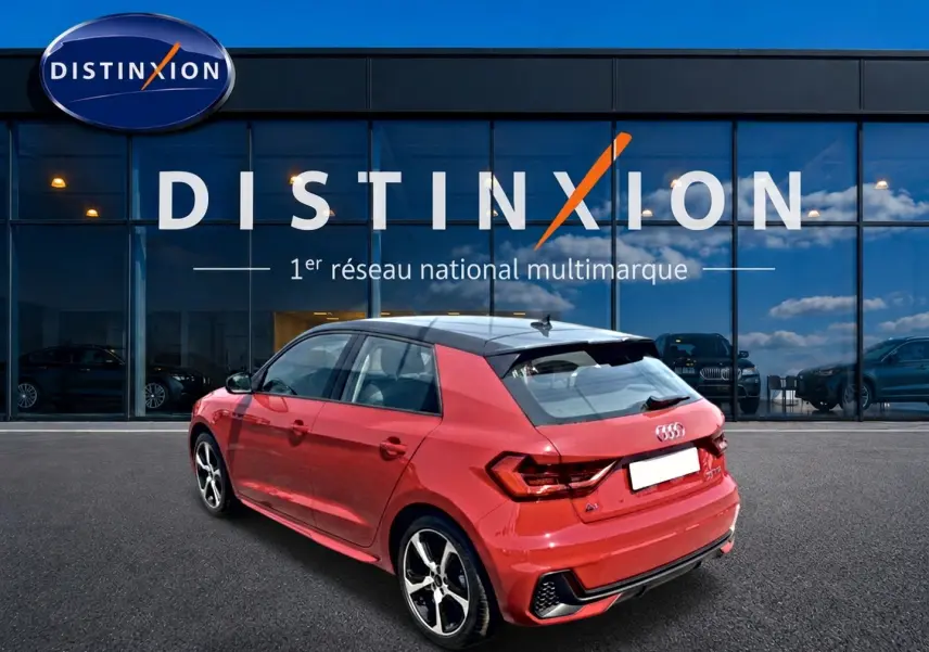 Audi A1 Sportback rouge et noir vue 3/4 arrière droit, avec jantes alu et becquet arrière visible devant une vitrine Distinxion.