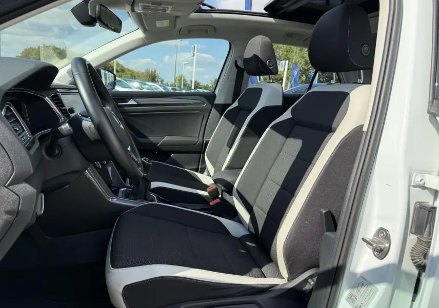 Vue intérieure côté gauche du Volkswagen T-Roc blanc 2022, montrant les sièges avant bicolores et le volant multifonction.