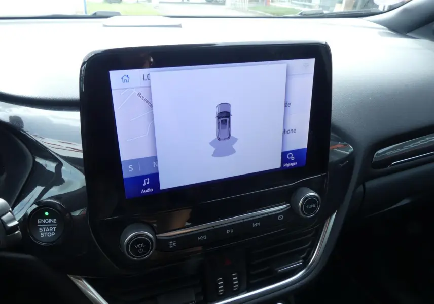 Vue rapprochée de la console centrale noire du Ford Puma 2020 avec écran tactile affichant une aide au stationnement.