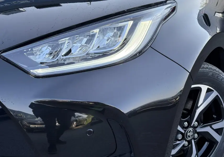 Gros plan sur le phare avant gauche et la jante alliage 16'' d'une Toyota Yaris Hybride 2025 noir intense.