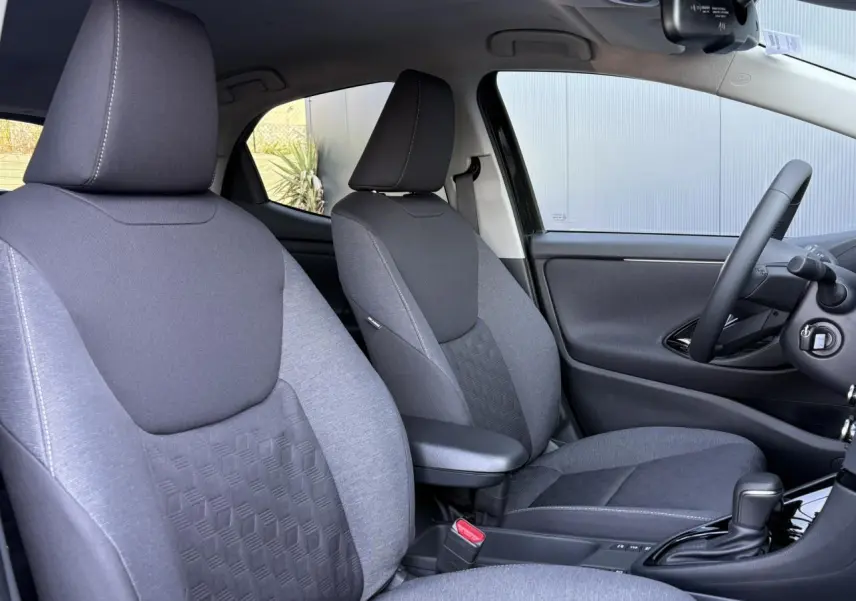 Intérieur de la Toyota Yaris Hybride 2025 vu côté droit, sièges gris et volant cuir avec console centrale noire.