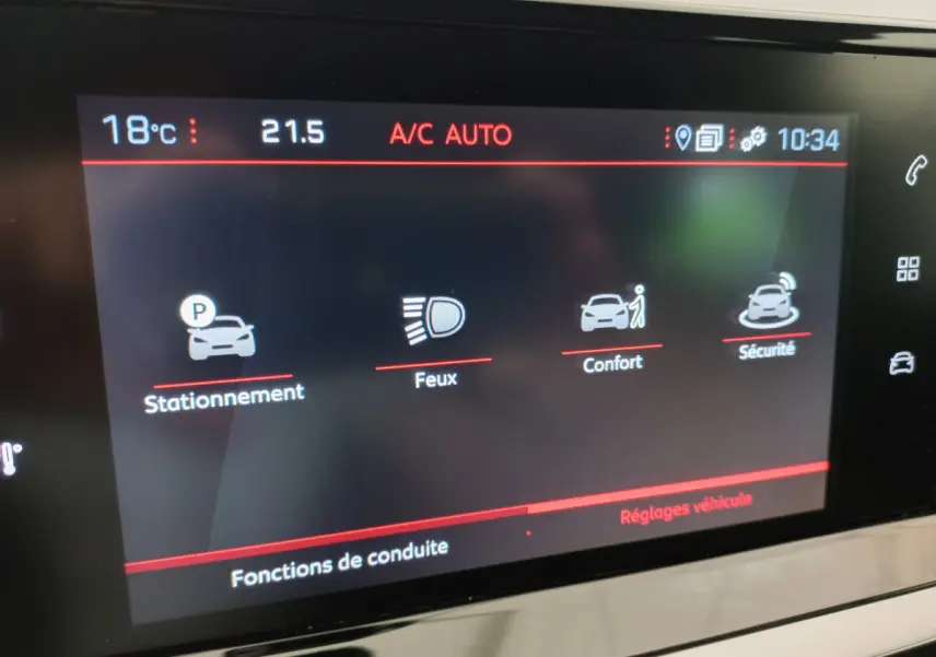 Écran tactile intérieur du tableau de bord de la Peugeot 208 blanc, affichant les réglages de conduite stationnement, feux, confort et sécurité.