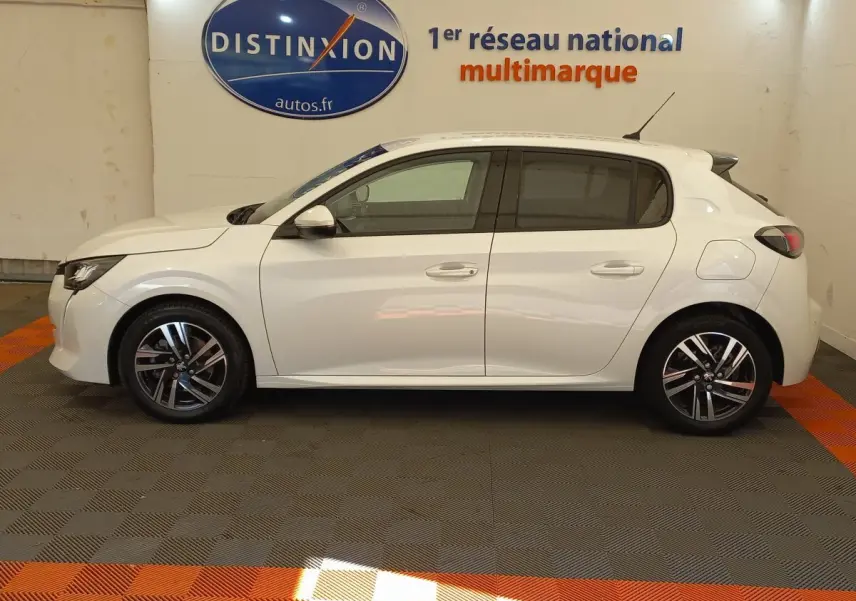 Profil côté gauche d'une Peugeot 208 blanche PureTech 100 S&S Allure 2021 dans un showroom avec sol gris et orange.