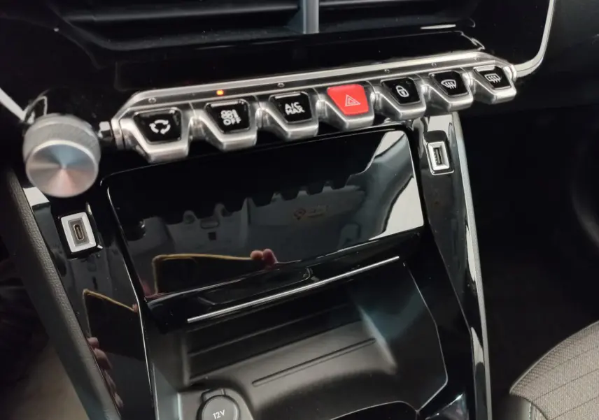 Gros plan sur la console centrale noire brillante de la Peugeot 208 PureTech 100 S&S Allure avec boutons de commande et ports USB visibles