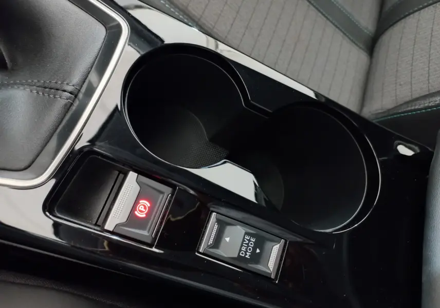 Gros plan sur la console centrale noire de la Peugeot 208 blanche, montrant frein à main électrique et bouton Drive Mode.