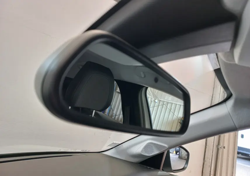 Rétroviseur intérieur gauche de la Peugeot 208 blanche, reflétant l'appui-tête et une porte de garage.