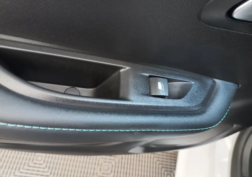 Gros plan sur la commande de lève-vitre côté gauche avec surpiqûres bleues dans l'habitacle d'une Peugeot 208 blanche.
