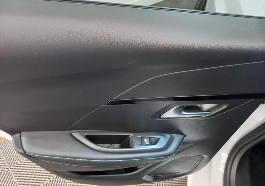 Gros plan sur la porte côté conducteur noire avec surpiqûres bleues d'une Peugeot 208 blanche 2021 PureTech Allure.