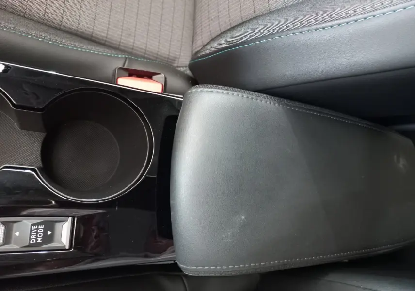 Gros plan sur l'accoudoir noir et le porte-gobelet central de la Peugeot 208 PureTech 100 S&S Allure blanche.