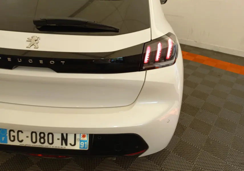 Vue arrière droite d'une Peugeot 208 blanche avec feux arrière LED allumés dans un garage.