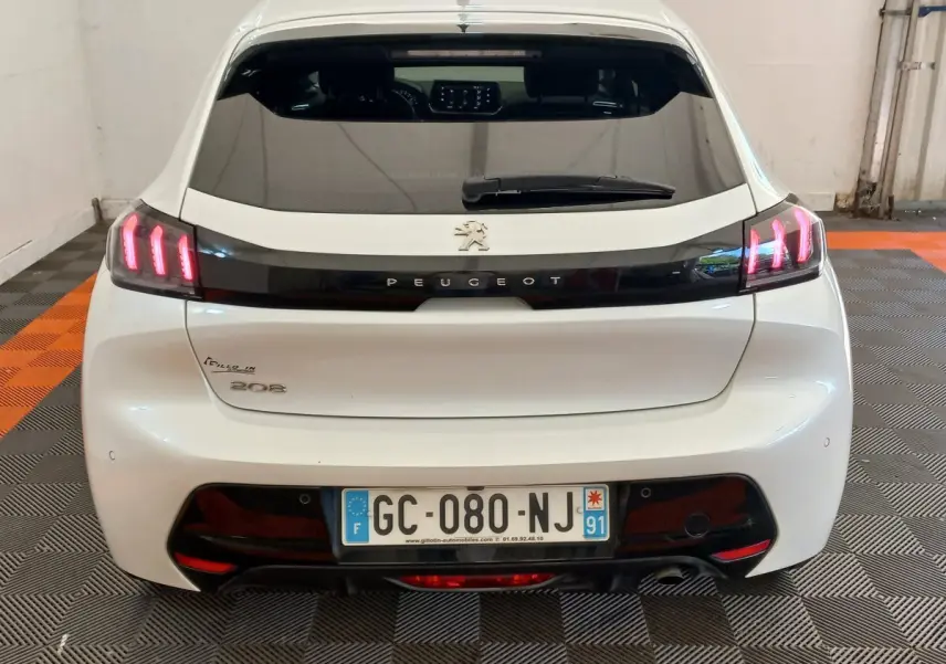 Vue arrière d'une Peugeot 208 blanche avec feux LED allumés et logo Peugeot visible sur le hayon.