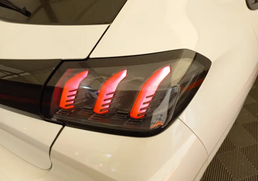 Gros plan sur le feu arrière droit rouge et noir d'une Peugeot 208 blanche PureTech 100 S&S Allure 2021.